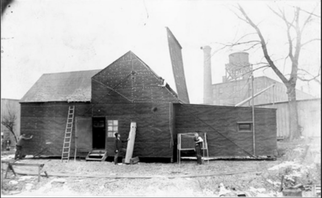 Wide shot of a large black shed. A section of the roof is open. A track surrounds the building.
