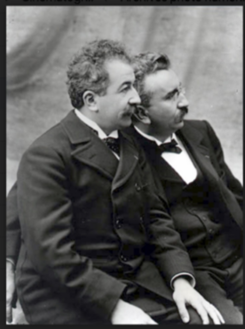 Auguste Lumière (left) and Louis Lumière (right), dressed in suits, seated, in profile.