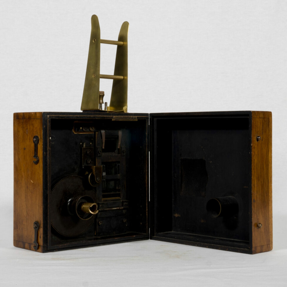 The wooden camera is open. The internal mechanism is visible. The body of the camera is this time surmounted by two metal rods which support the positive film.