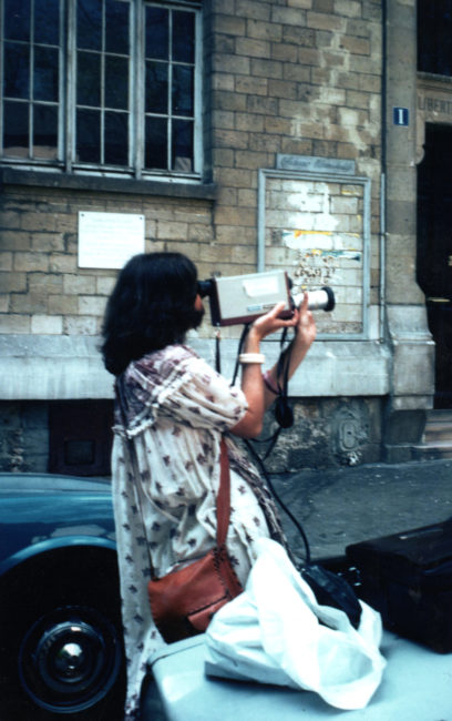 Nicole tient la caméra sans trépied. L’œil collé au viseur, main droite sous la caméra et main gauche sur le zoom. L’enregistreur est posé sur une voiture à côté de la réalisatrice.