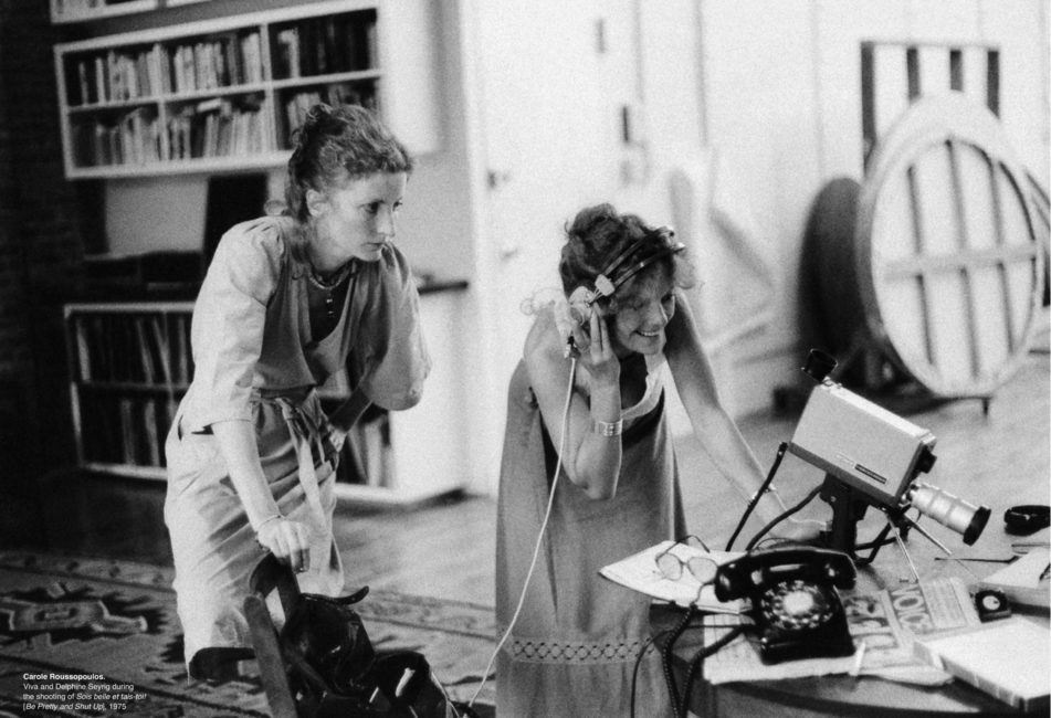 Two women watch a take through the camera. The woman on the right wears headphones to listen while she watches.